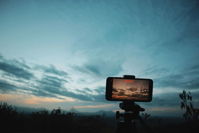 Smartphone sobre tripode grabando un cielo nublado al atardecer sobre un paisaje de montana