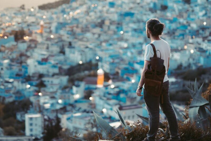 Viajero con mochila de espaldas contemplando la ciudad azul de Chefchaouen al atardecer, Marruecos