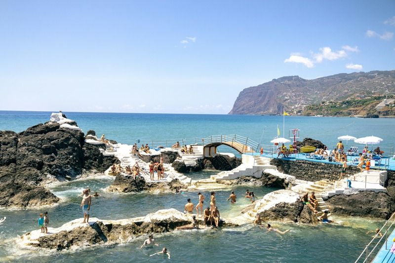 Turistas bañándose en las piscinas naturales de roca volcánica de Porto Moniz, Madeira, con el mar al fondo
