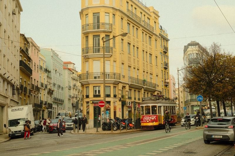 Tranvía histórico rojo pasando por una calle de Lisboa junto a un edificio de esquina amarillo en el barrio histórico de la ciudad