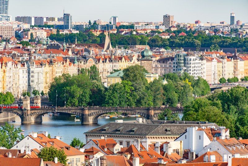 Vista aérea de Praga con tejados rojos, el río Moldava y los puentes históricos de la ciudad iluminados por el sol