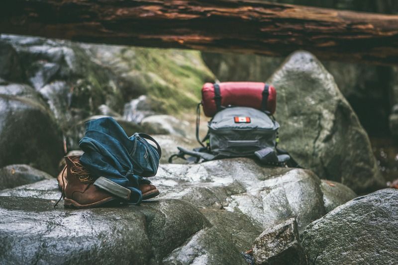 Botas de senderismo, vaqueros enrollados y una mochila de camping apoyados sobre rocas en el bosque