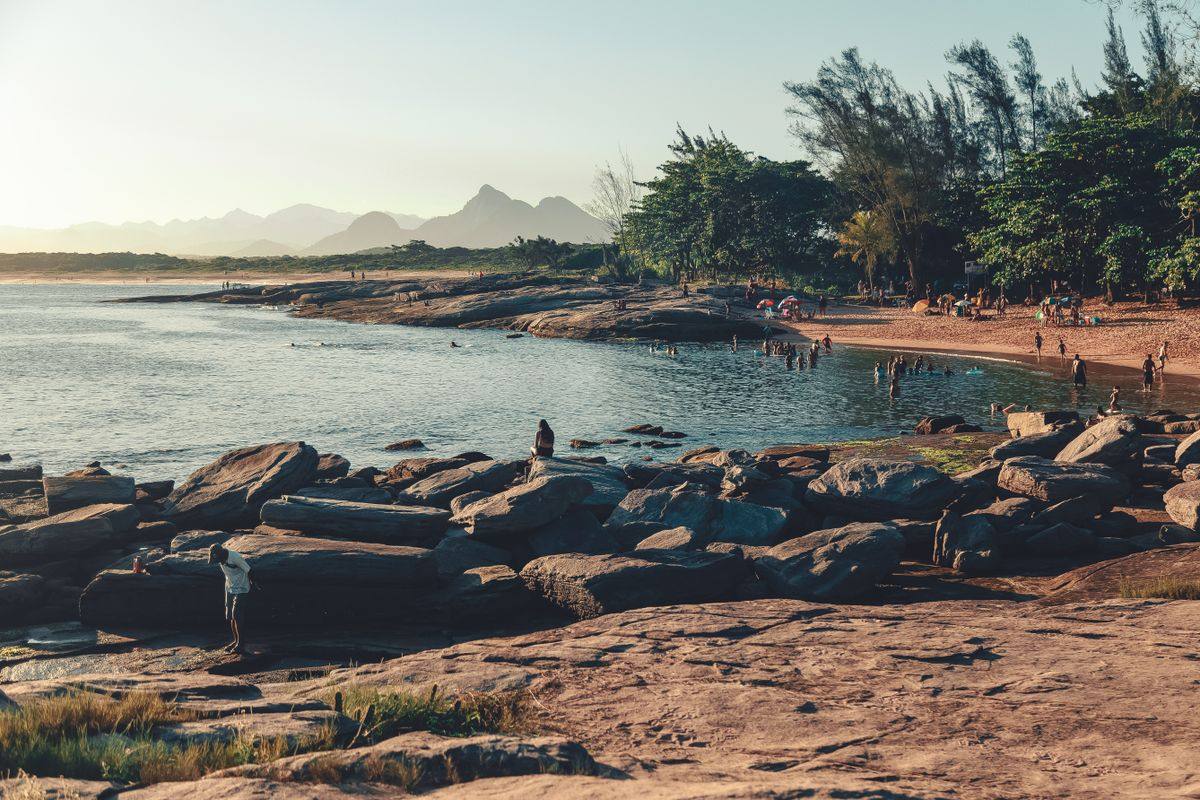 Costa rocosa con personas junto al agua, playa estrecha y árboles frente al mar