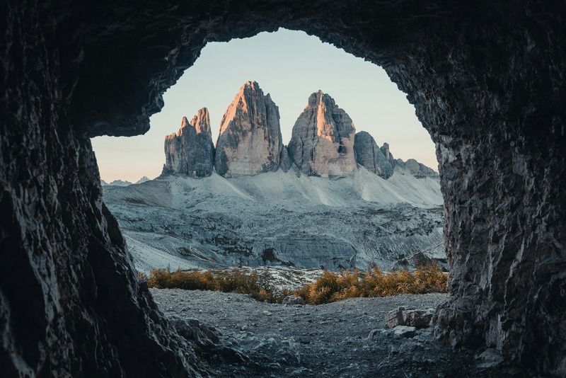 Vista de las Tre Cime di Lavaredo enmarcada por la boca de una cueva rocosa en los Dolomitas durante la hora dorada