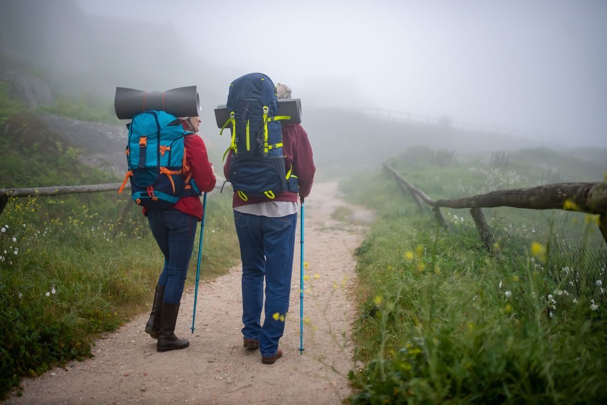 Dos excursionistas con grandes mochilas caminan por un sendero con niebla