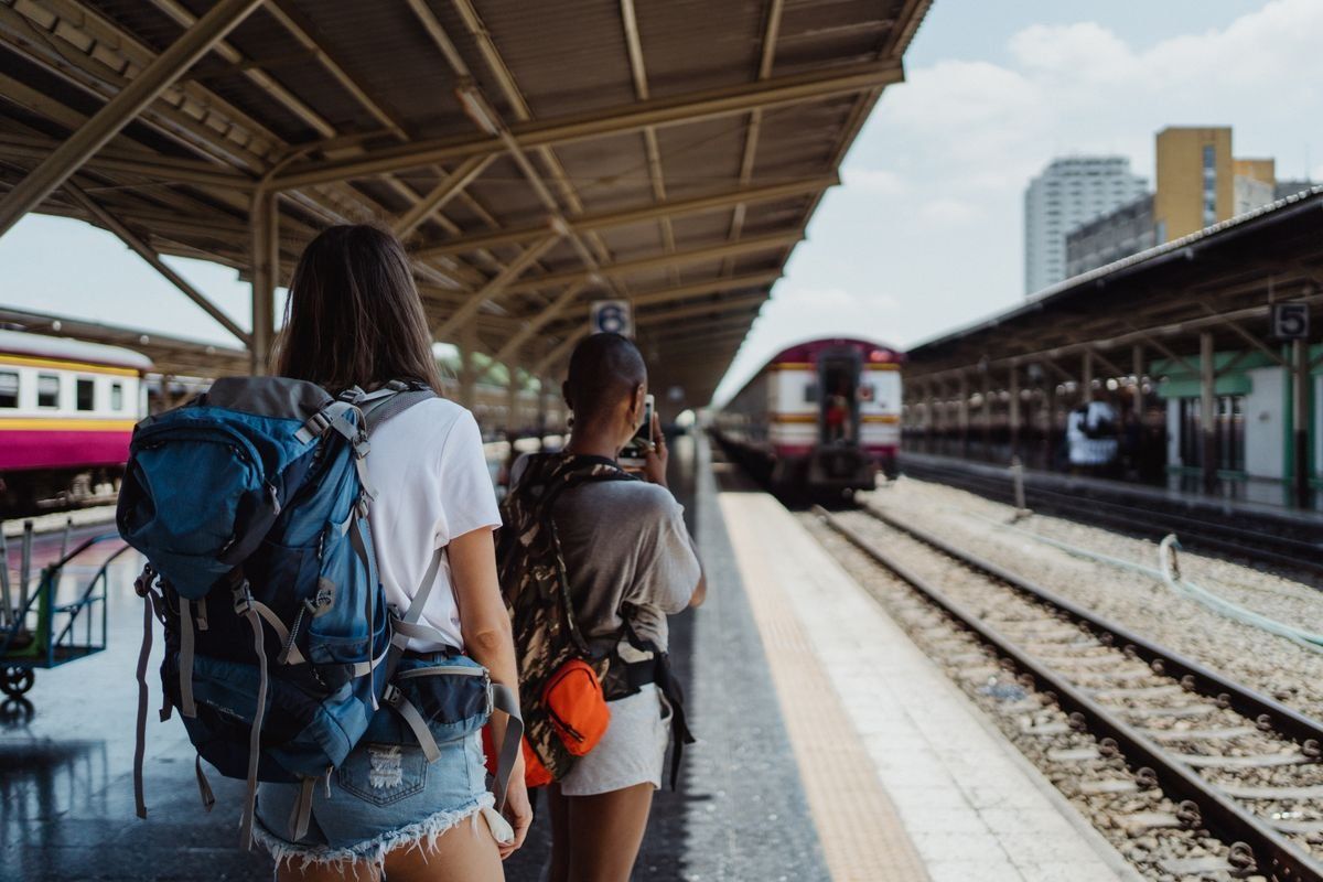 Dos mochileras esperan en un andén de tren con sus mochilas