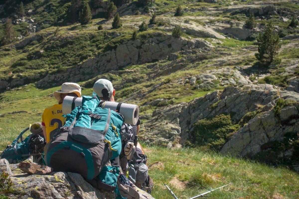 Dos senderistas con mochilas descansan sobre la hierba en una ladera de montaña