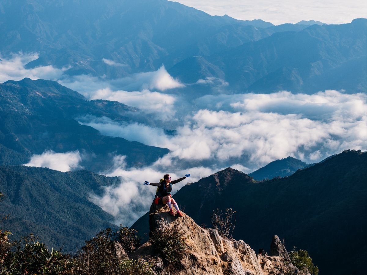 Excursionista sobre una roca en la cima con montañas y nubes alrededor