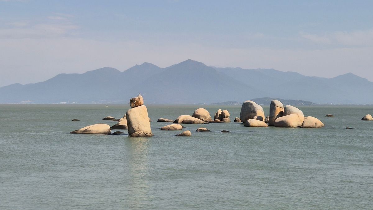Grandes rocas en un mar tranquilo con montañas difusas al fondo bajo cielo despejado