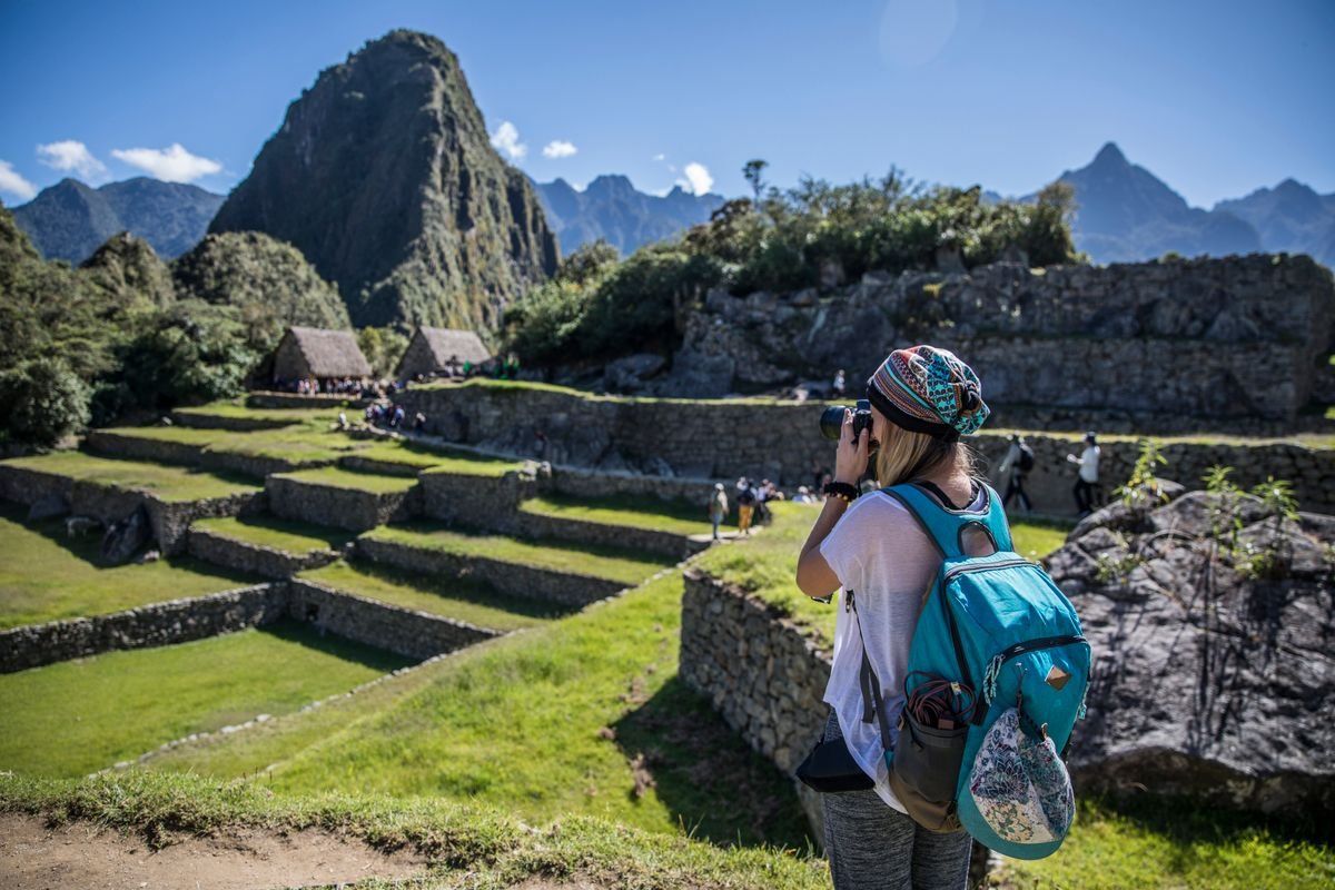 Mujer con mochila fotografiando Machu Picchu en un día soleado
