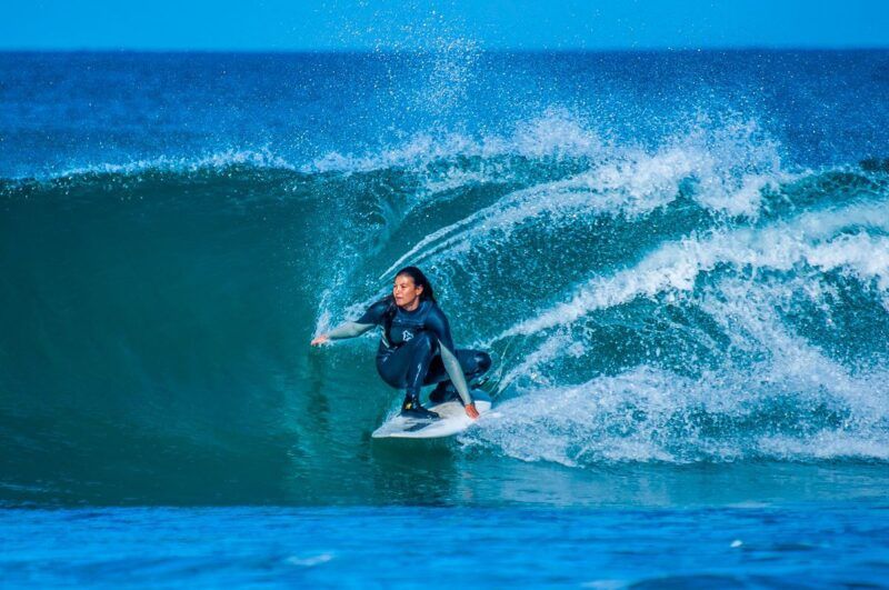Mujer surfista trazando un giro sobre una ola grande y azul.