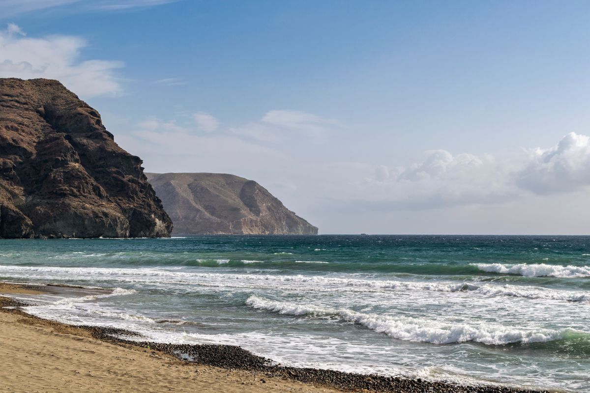 Playa con oleaje suave, arena y colinas rocosas bajo un cielo despejado
