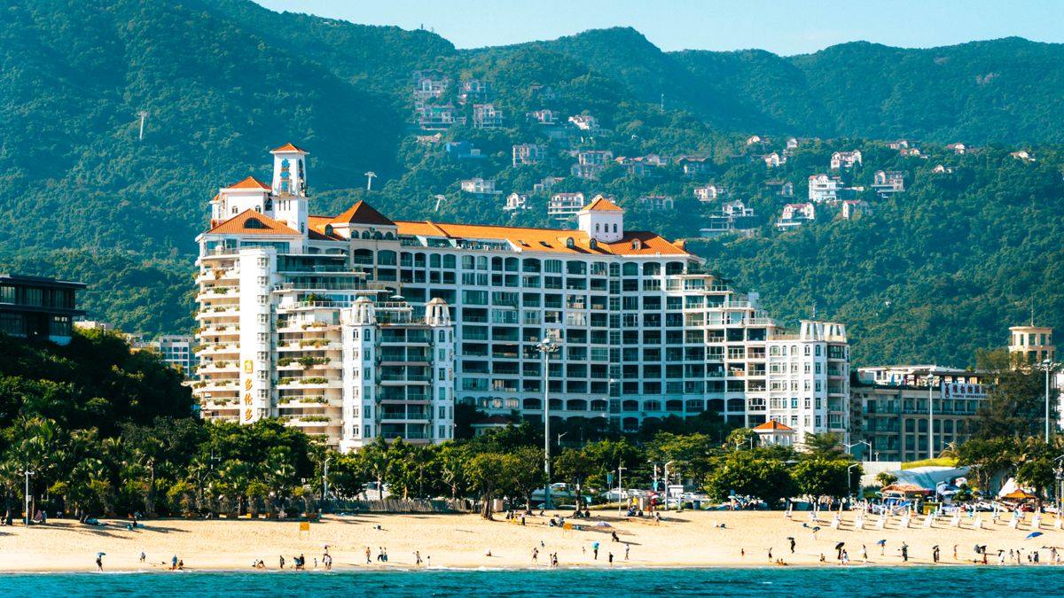 Resort frente a la playa con edificios blancos y montañas cubiertas de vegetación al fondo