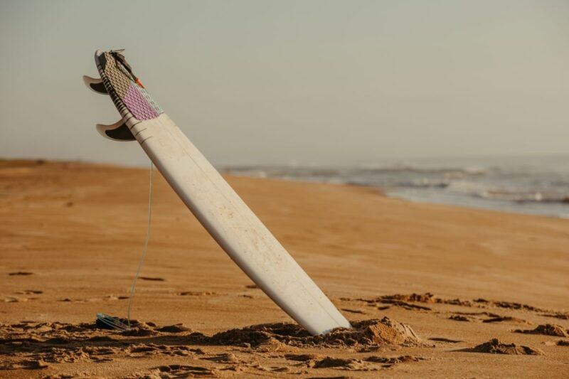 Tabla de surf clavada en la arena de una playa vacía.