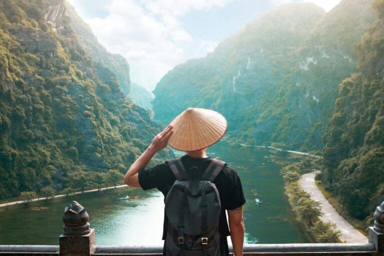 Viajero de espaldas con sombrero cónico vietnamita contempla el valle kárstico de Trang An, Vietnam