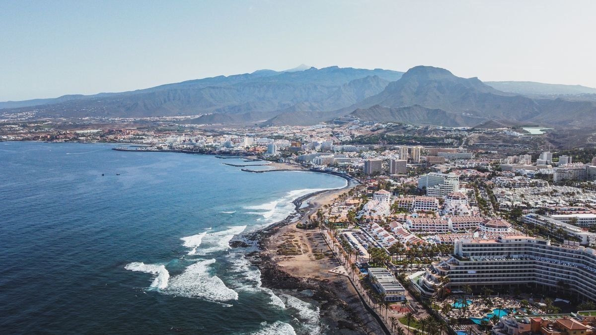 Vista aérea de costa urbana con hoteles, playa, rompientes y montañas al fondo