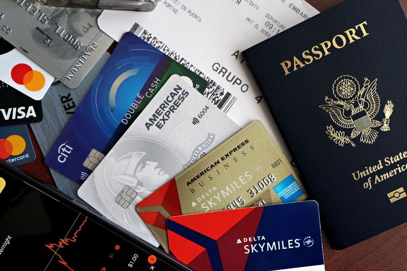 Una composición con un pasaporte estadounidense, una tarjeta de embarque y varias tarjetas de crédito junto a un móvil con un gráfico bursátil