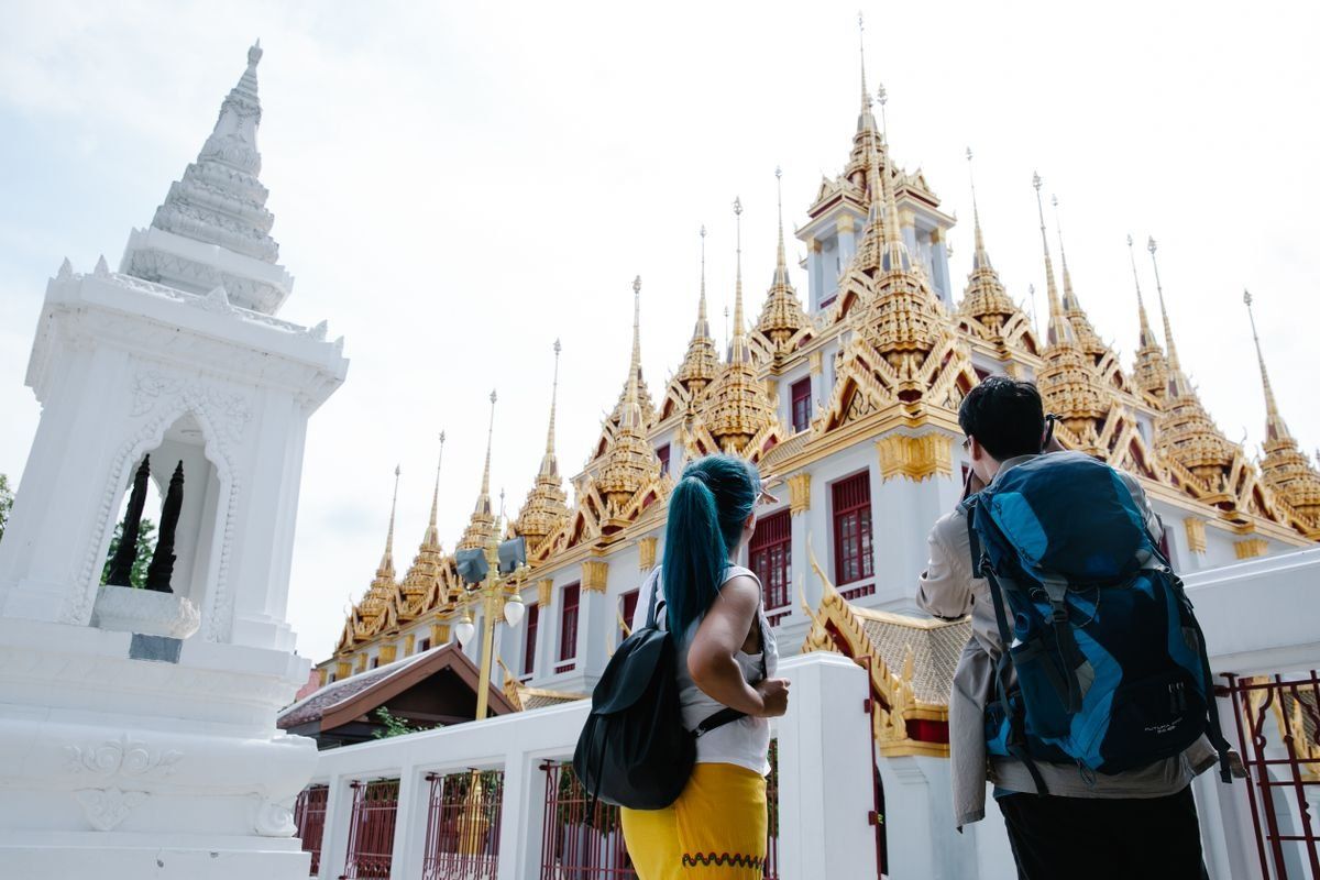 Dos viajeros con mochilas observan la fachada ornamentada de un templo tailandés