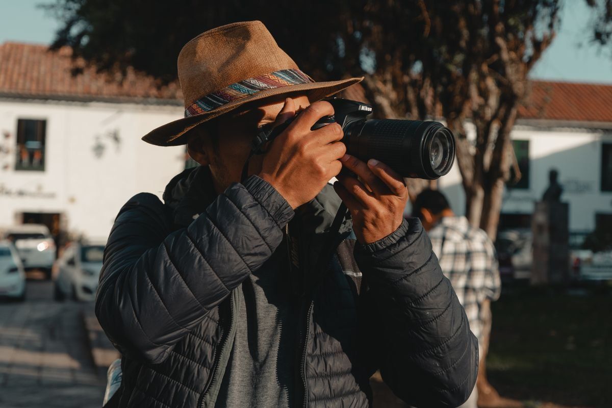 Hombre con sombrero fedora tomando una foto con cámara al aire libre