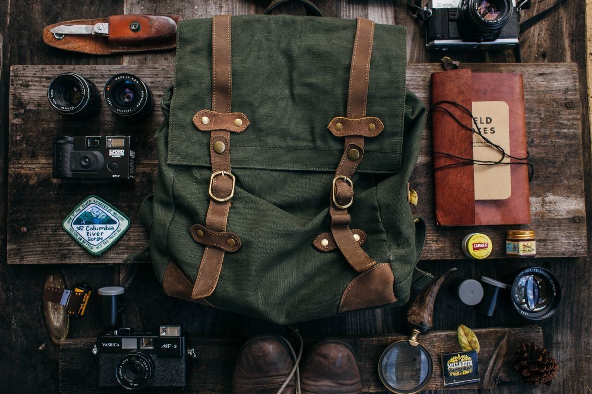 Mochila verde sobre mesa de madera rodeada de cámaras, cuaderno y accesorios
