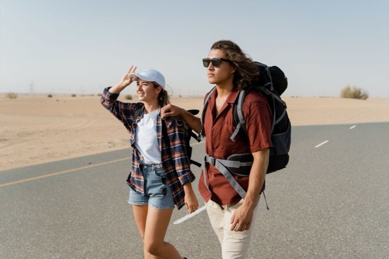 Pareja con mochilas caminando por una carretera del desierto