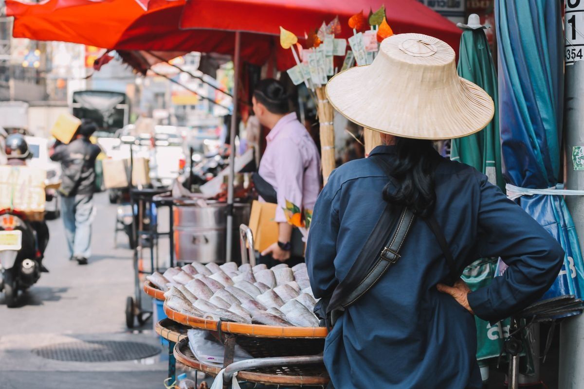 Vendedora con sombrero junto a pescado en un mercado callejero bajo sombrillas rojas
