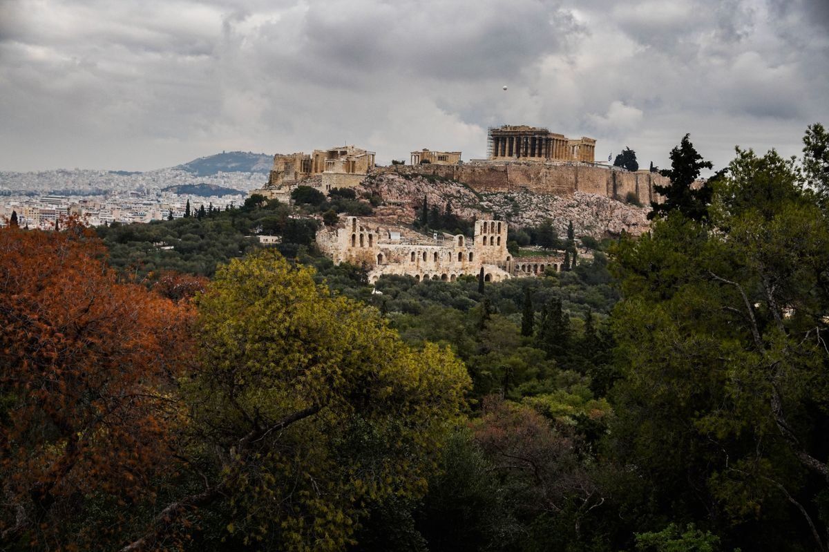 Acrópolis de Atenas sobre la colina con árboles en primer plano y cielo nublado