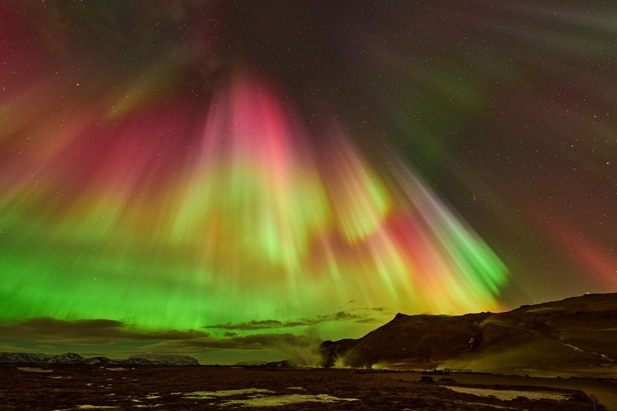 Aurora boreal verde y roja sobre colinas oscuras en un paisaje nocturno