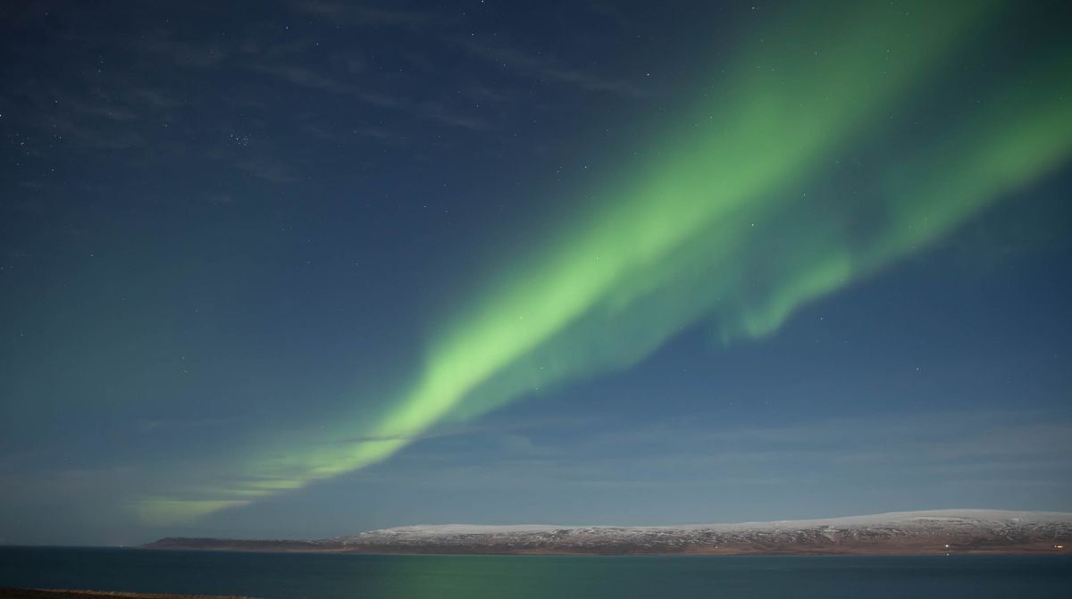 Aurora boreal verde sobre el mar tranquilo y una costa nevada al fondo