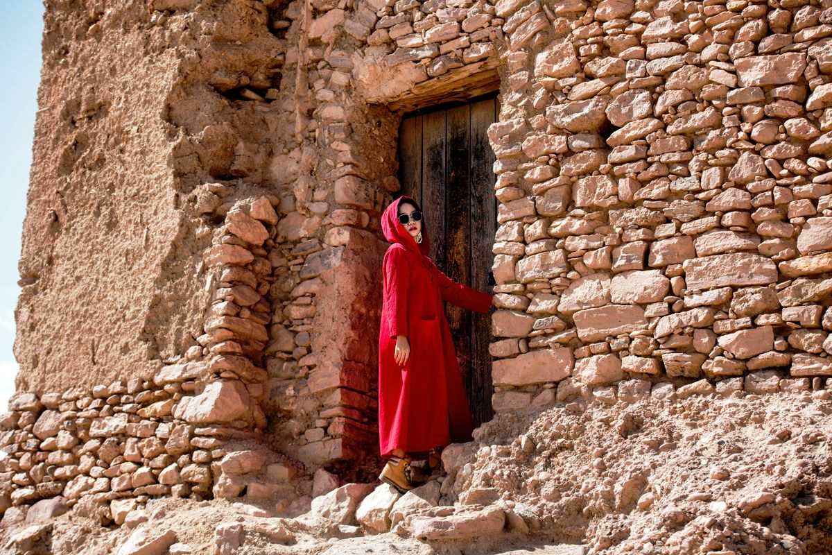 Mujer con abrigo rojo junto a una puerta en un muro de piedra