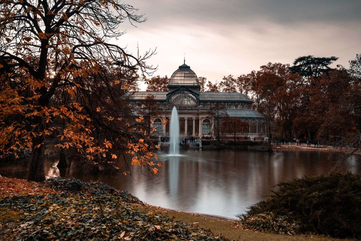 Palacio de Cristal de Madrid frente al estanque con fuente y árboles de otoño