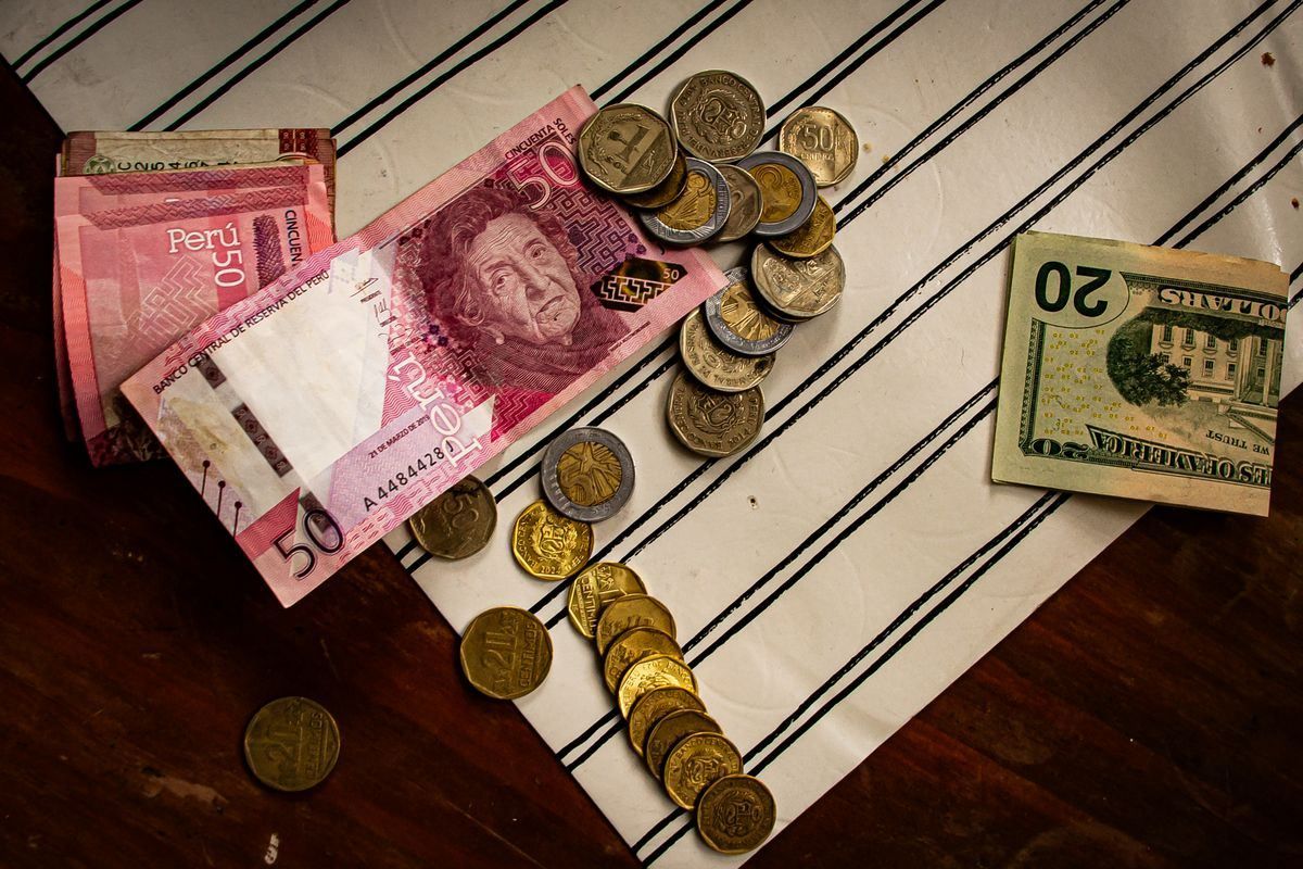 Billetes peruanos y un dólar estadounidense con monedas sobre una superficie a rayas