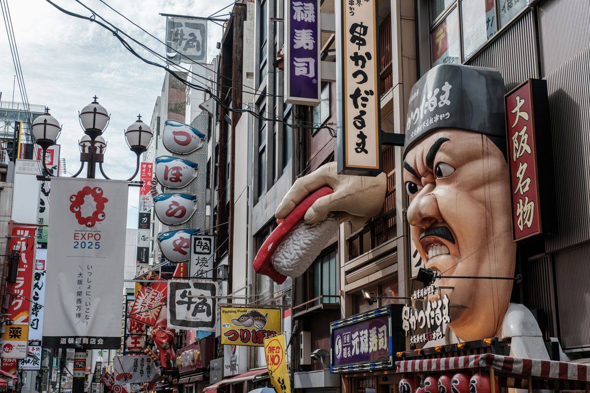 Calle comercial de Osaka con carteles verticales, faroles y un gran rótulo con cara y sushi