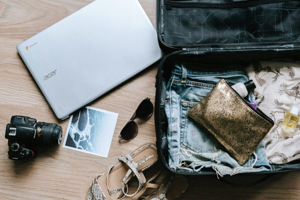 Cámara, gafas de sol, portátil y maleta abierta listos para el viaje
