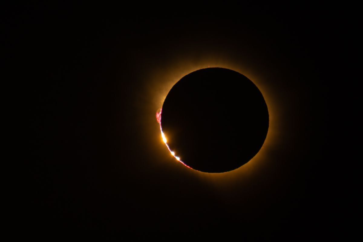 Eclipse total de Sol con corona tenue y destellos brillantes en el borde