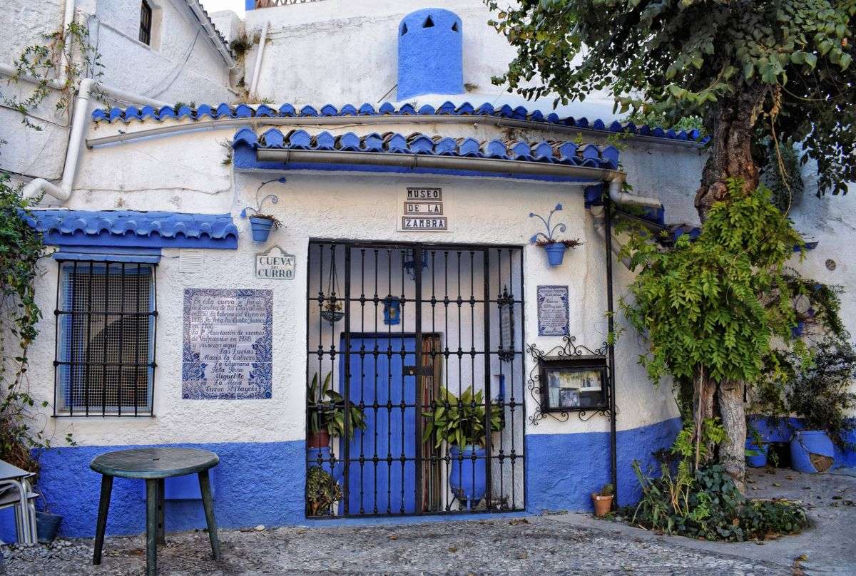 Fachada blanca y azul del Museo de la Zambra con puerta enrejada y árbol lateral