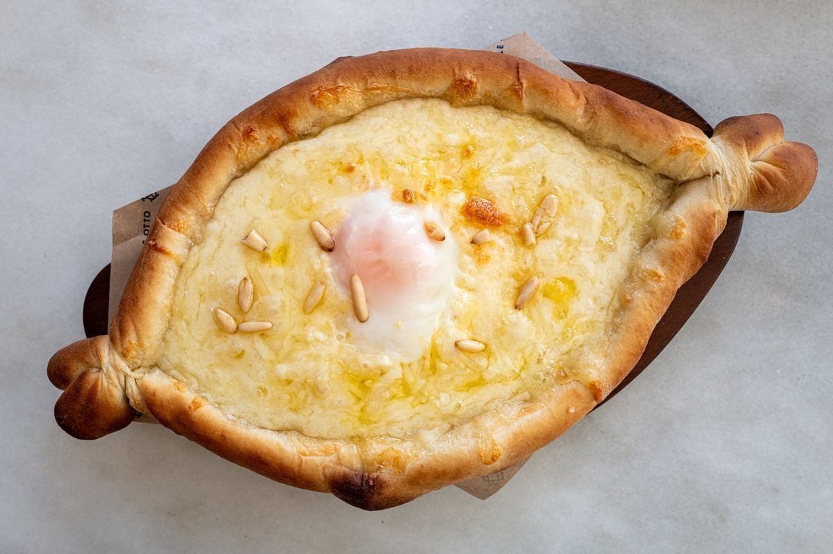 Khachapuri en forma de barca con queso, huevo y piñones sobre superficie clara
