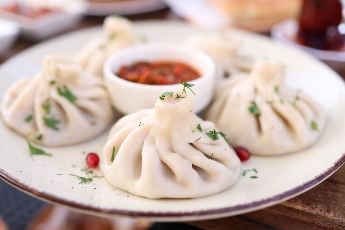 Khinkali servidos en plato blanco con salsa roja en cuenco central
