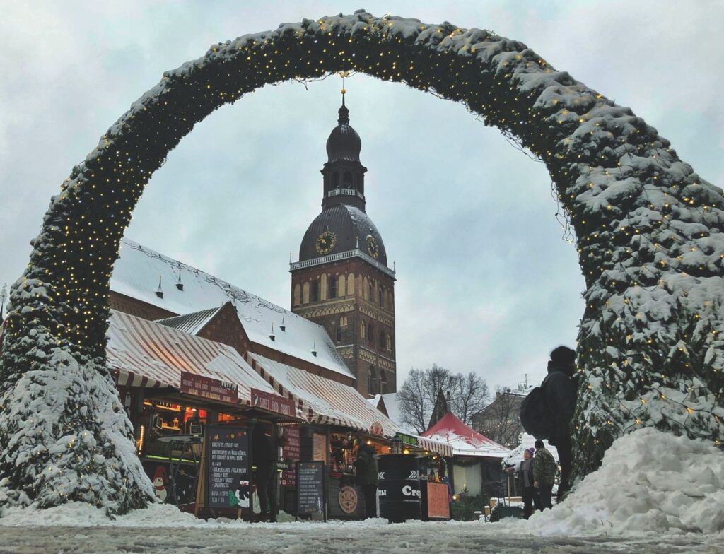Arco nevado y casetas del mercado de Navidad frente a la catedral de Riga