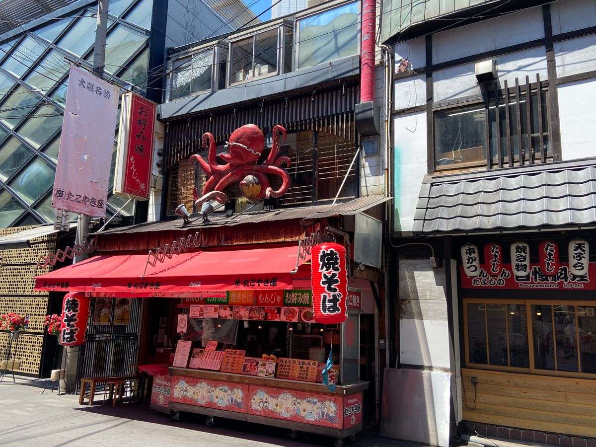 Puesto callejero con toldo rojo y una gran figura de pulpo sobre la fachada