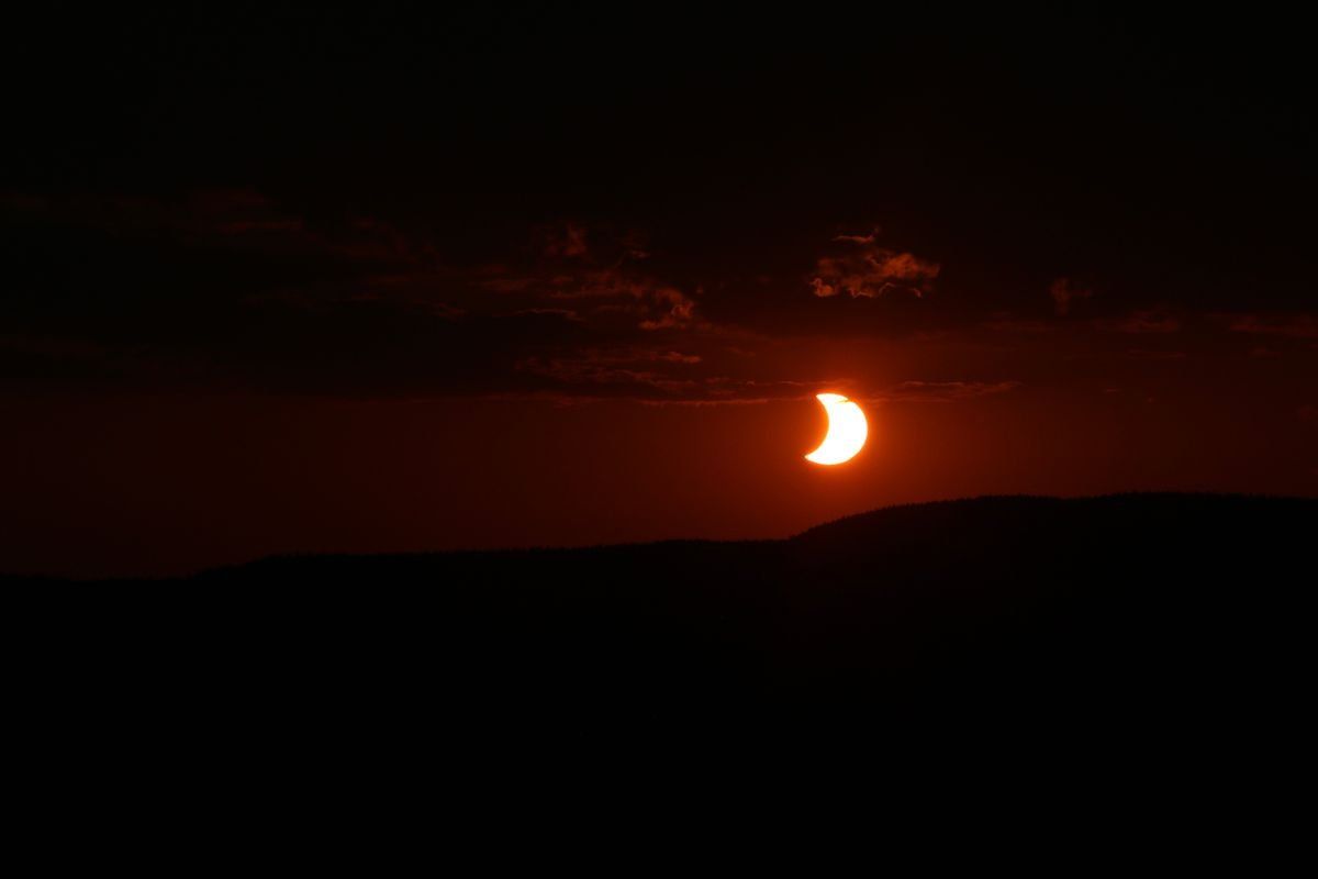 Sol eclipsado al atardecer sobre colinas en silueta y cielo rojizo