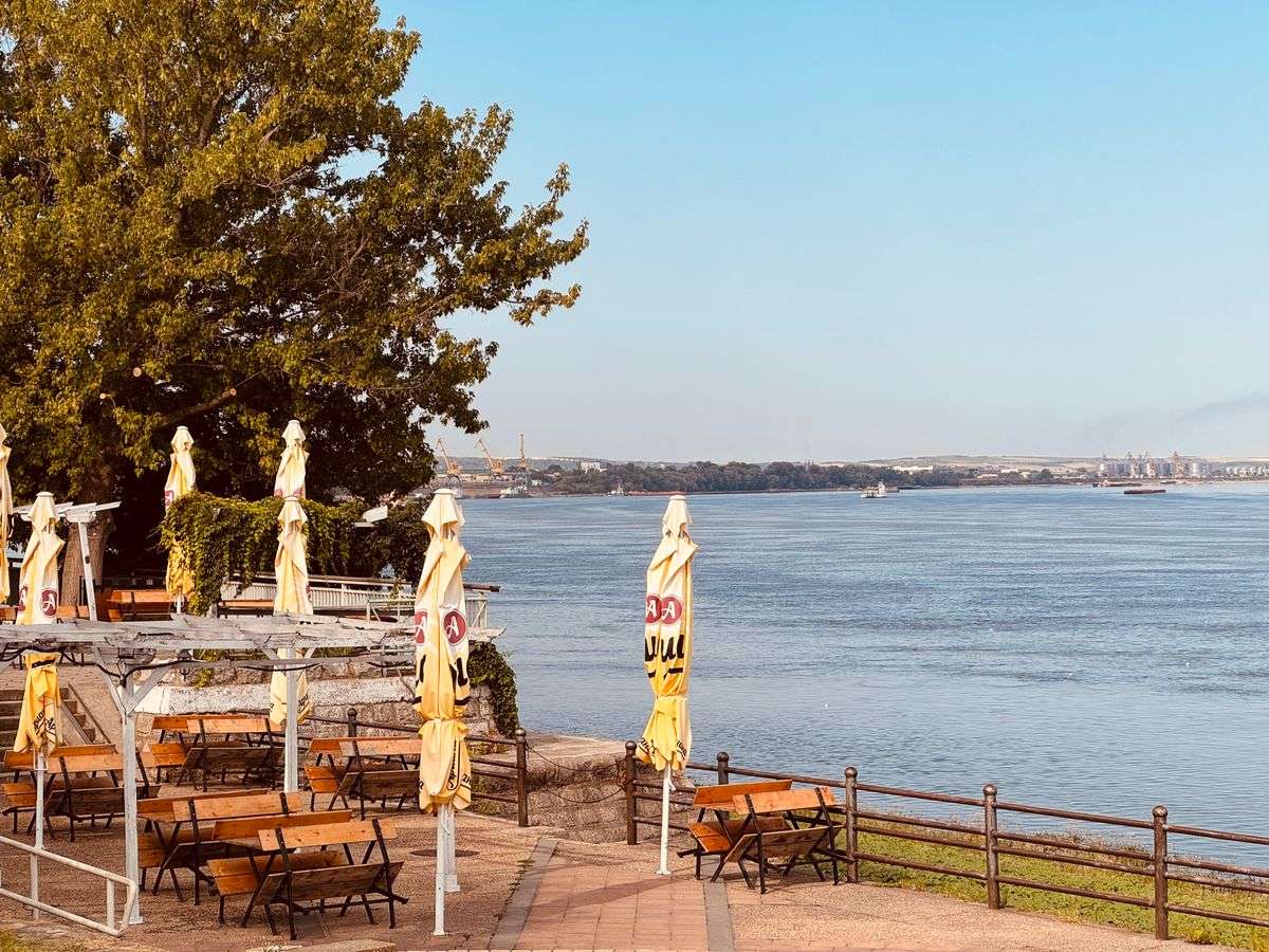Terraza junto al río con mesas vacías y sombrillas cerradas frente al agua